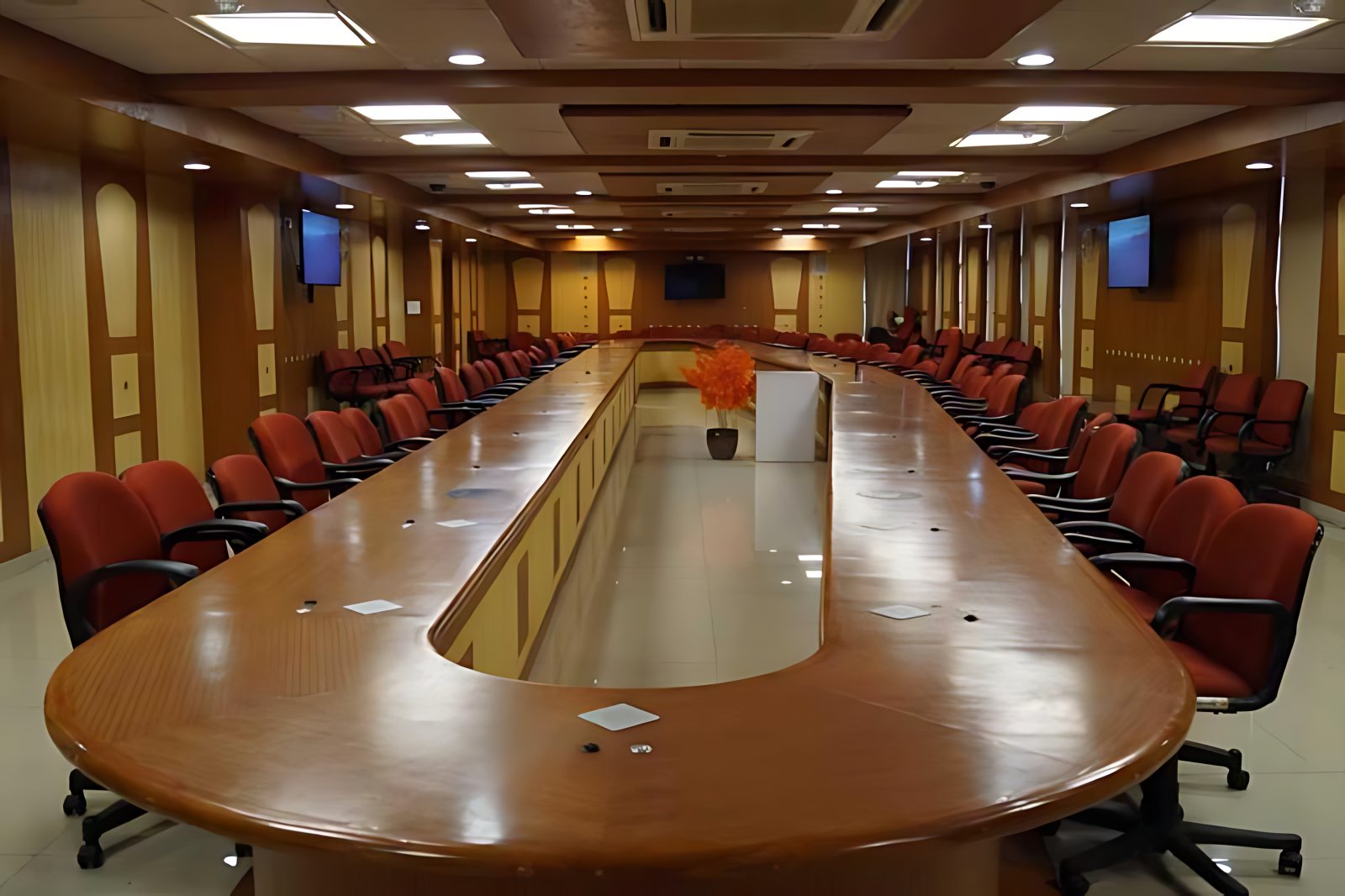 BSNL boardroom: a long oval table with red chairs and wall-mounted displays